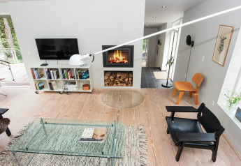 Modernes Wohnzimmer in einem Ferienhaus in Ebeltoft mit Kamin, Glastisch, Bücherregal und Designerstühlen.