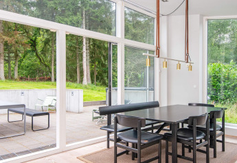 Comedor de casa de vacaciones moderna en Ebeltoft, Dinamarca, con grandes ventanales y vistas verdes.