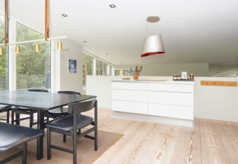 Sala da pranzo moderna e cucina in casa vacanze per 8 persone a Ebeltoft, Danimarca, con vista sul bosco.