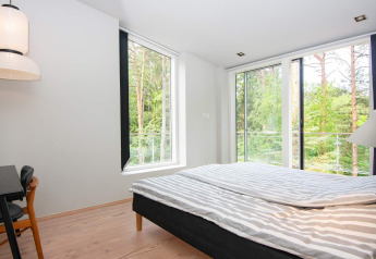 Camera da letto con arredamento moderno, grandi finestre e vista sul bosco in una casa vacanze a Ebeltoft, Danimarca.