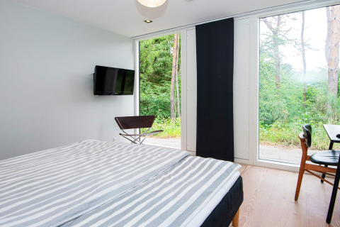 Schlafzimmer mit Doppelbett, Fernseher, Stühlen und Panoramafenstern in einer Ferienwohnung in Ebeltoft.