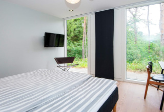 Schlafzimmer mit Doppelbett, Fernseher, Stühlen und Panoramafenstern in einer Ferienwohnung in Ebeltoft.