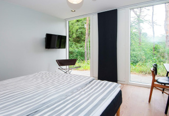 Camera da letto con letto matrimoniale, TV, sedie e grandi finestre con vista foresta in Ebeltoft.