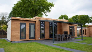 Moderne glamping accommodatie met houten buitenkant en overdekt terras met eettafel in groene omgeving.