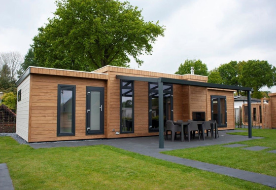 Alojamiento de glamping moderno con fachada de madera y terraza cubierta, situado en un entorno verde.