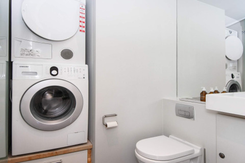 Modernes Badezimmer in Ebeltoft mit Waschmaschine, Trockner, Toilette und Spiegel in heller Einrichtung.