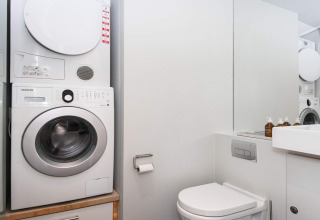 Modernes Badezimmer in Ebeltoft mit Waschmaschine, Trockner, Toilette und Spiegel in heller Einrichtung.