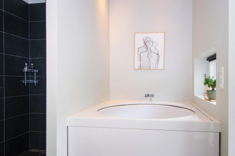 Modernes Badezimmer im 8-Personen-Ferienhaus in Ebeltoft, Dänemark mit Badewanne, Dusche und Wandkunst.