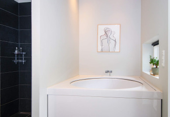 Baño moderno en casa vacacional para 8 personas en Ebeltoft, Dinamarca, con bañera, ducha y arte minimalista.