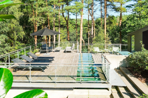 Sonnige Dachterrasse mit Liegen, Glasboden, Sonnenschirm und Waldblick am Ferienhaus in Ebeltoft, Dänemark.