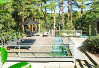 Sonnige Dachterrasse mit Liegen, Glasboden, Sonnenschirm und Waldblick am Ferienhaus in Ebeltoft, Dänemark.