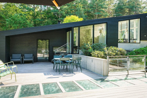 Modernes Ferienhaus in Ebeltoft, Dänemark, mit großer Terrasse, Gartenmöbeln und Wald im Hintergrund.