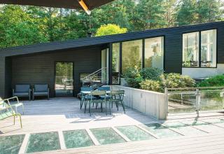 Modernes Ferienhaus in Ebeltoft, Dänemark, mit großer Terrasse, Gartenmöbeln und Wald im Hintergrund.