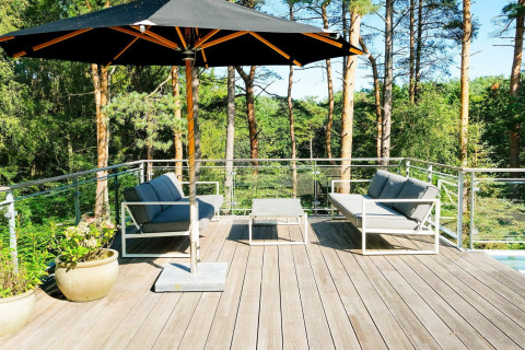 Terrasse eines 8-Personen-Ferienhauses in Ebeltoft, Dänemark, mit Sitzmöbeln, Sonnenschirm und Waldblick.