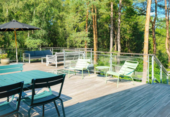 Ruim houten terras met tuinmeubilair en glazen balustrade bij een bos bij '8-persoons vakantiewoning in Ebeltoft', Denemarken.