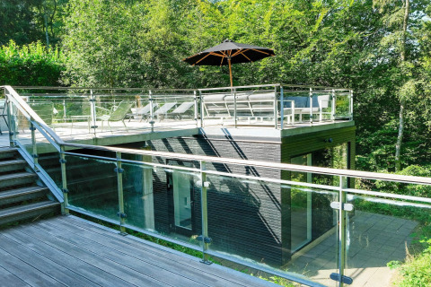 Modernes Ferienhaus in Ebeltoft, Dänemark mit Glasgeländer, Dachterrasse und Liegestühlen im Grünen.