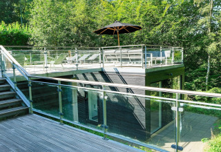 Modernes Ferienhaus in Ebeltoft, Dänemark mit Glasgeländer, Dachterrasse und Liegestühlen im Grünen.