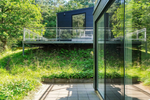 Modernes Ferienhaus mit Glasbalkon inmitten grüner Natur in Ebeltoft, Dänemark, sonniger Tag.