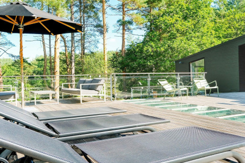Sonnige Terrasse mit Liegestühlen, Sitzgruppe und Glasgeländer an einer Ferienhütte für 8 Personen in Ebeltoft, Dänemark.