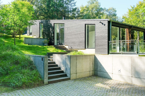 Modernes Ferienhaus in Ebeltoft, Dänemark, mit schwarzer Holzfassade und großen Glasfenstern im Grünen.