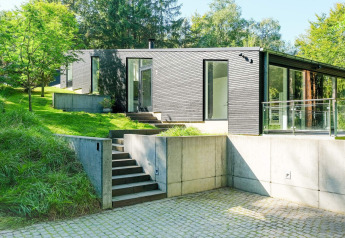 Maison de vacances moderne à Ebeltoft, Danemark, façade noire, grandes fenêtres, entourée de verdure.