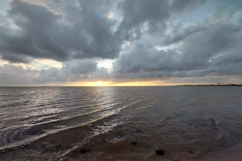 Zonsondergang boven zee bij Secluded Harbor Cottage in Denemarken, met dramatische wolken en kalm water.