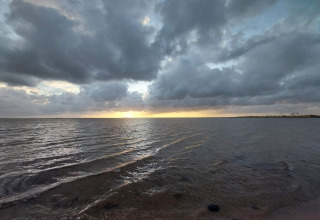 Zonsondergang boven zee bij Secluded Harbor Cottage in Denemarken, met dramatische wolken en kalm water.