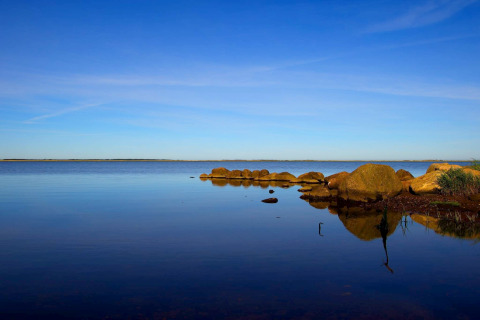 Rustig uitzicht op het meer bij de lodge met een heldere blauwe lucht en grote stenen aan de oever.