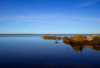 Rustig uitzicht op het meer bij de lodge met een heldere blauwe lucht en grote stenen aan de oever.