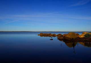 Ruhiges Seepanorama an einer Lodge mit klarblauem Himmel und Felsen am Wasserrand im Vordergrund.