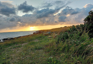 Sonnenuntergang an einer Lodge mit grasbewachsener Küste, Steinen und dichter Bewölkung im Hintergrund.