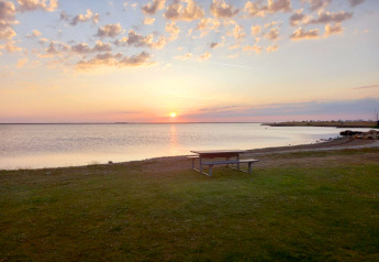 Solnedgang ved kysten med picnicbord på græsplæne foran Secluded Harbor Cottage i Danmark.