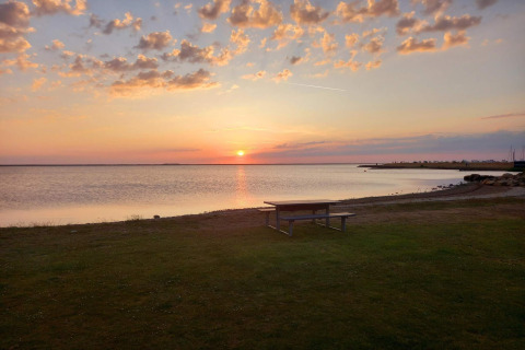Sonnenuntergang am Wasser mit Picknicktisch auf Wiese vor Secluded Harbor Cottage in Dänemark.