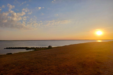 Zonsondergang boven rustig water gezien vanaf Secluded Harbor Cottage in Denemarken, gouden lucht en kust.