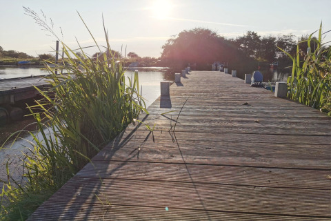Zonsondergang op een houten steiger bij Secluded Harbor Cottage in Denemarken, omgeven door riet en water.
