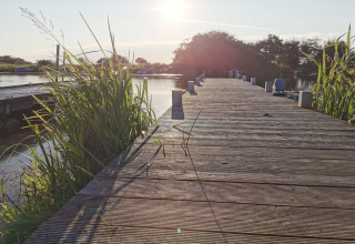 Zonsondergang op een houten steiger bij Secluded Harbor Cottage in Denemarken, omgeven door riet en water.