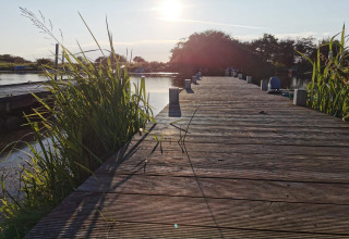 Zonsondergang op een houten steiger bij Secluded Harbor Cottage in Denemarken, omgeven door riet en water.