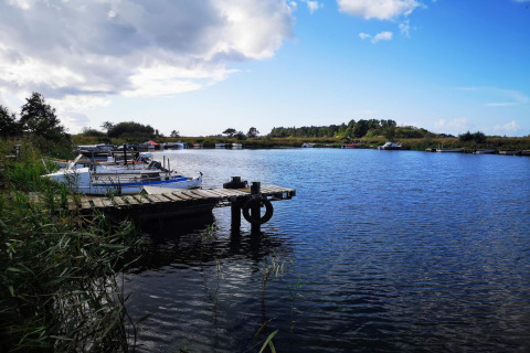 Houten steiger en boten op een rustig meer met blauwe lucht bij een lodge omringd door natuur.