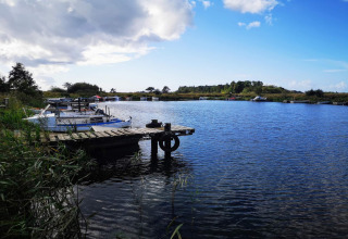 Houten steiger en boten op een rustig meer met blauwe lucht bij een lodge omringd door natuur.