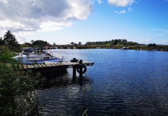 Pontile in legno e barche su un lago calmo con cielo azzurro vicino a un lodge immerso nella natura.