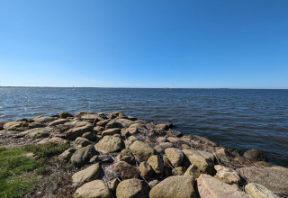 Blick auf einen ruhigen See mit steinigem Ufer und blauem Himmel am Secluded Harbor Cottage in Dänemark.