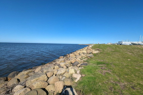 Küstenlandschaft bei Secluded Harbor Cottage in Dänemark mit blauem Himmel, Felsen und Booten.
