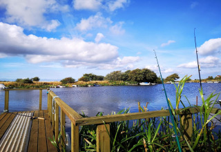 Uitzicht vanaf een lodge met vislijnen en houten terras, uitkijkend over een rustige rivier en groene bomen.