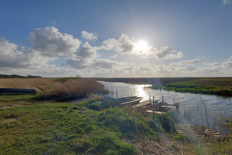 Vue ensoleillée d'une rivière avec des barques près d'un lodge, entourée de verdure et de nature.