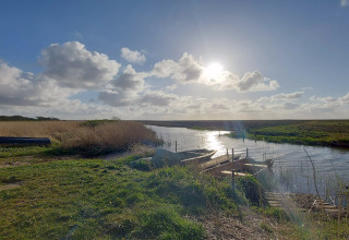 Vue ensoleillée d'une rivière avec des barques près d'un lodge, entourée de verdure et de nature.