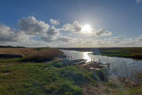 Vue ensoleillée d'une rivière avec des barques près d'un lodge, entourée de verdure et de nature.