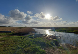 Sonnenbeschienene Szene mit Fluss, Booten und Steg, umgeben von grüner Natur an einer Lodge.