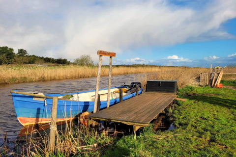 Blauwe boot aangemeerd aan een houten steiger bij Secluded Harbor Cottage, Denemarken, omringd door natuur.