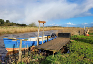 Blauwe boot aangemeerd aan een houten steiger bij Secluded Harbor Cottage, Denemarken, omringd door natuur.
