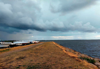 Boten liggen langs de oever bij de lodge, onder een bewolkte hemel boven een grasachtig pad en het meer.